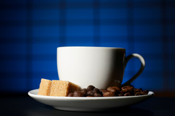 A Cup of coffee with a piece of cane sugar in a saucer on a blue background