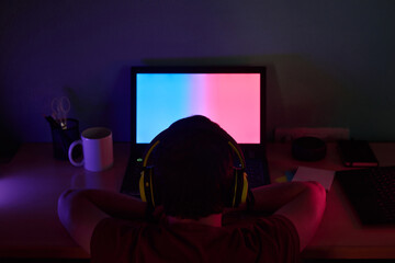 Young man looks his screen laptop illuminated with colored lights