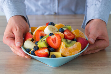 Fresh Fruit Salad, The man holds a plate full of sliced fruit over the table
