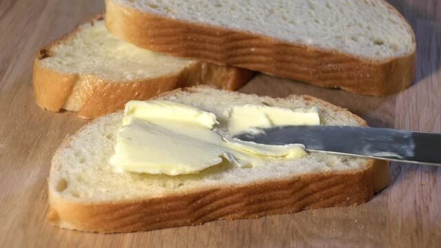 A piece of white bread and butter rotates on a grey background