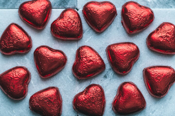 Red hearts on a marble surface, chocolates in red tin foil
