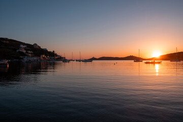 Fototapeta na wymiar Sunset orange color over sea water. Boats anchored at Vourkari port, Kea island, Greece.