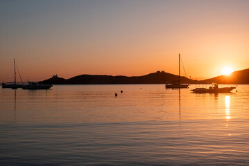 Sunset orange color over sea water. Boats anchored at Vourkari port, Kea island, Greece.