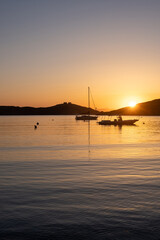 Fototapeta premium Sunset orange color over sea water. Boats anchored at Vourkari port, Kea island, Greece.