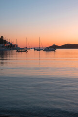 Naklejka premium Sunset orange color over sea water. Boats anchored at Vourkari port, Kea island, Greece.
