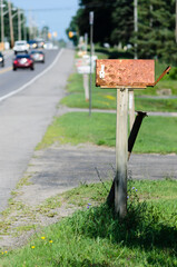 Rusty rural mailbox next to traffic on a road.