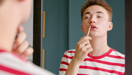 Young man doing make up lipstick or lip gloss and paints lips prepare getting ready in the morning....