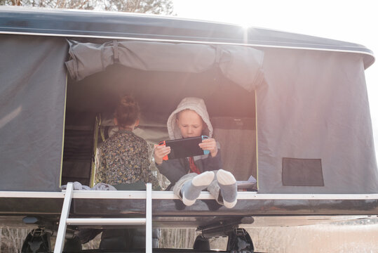 boy sat playing a Nintendo games console in a roof top tent camping
