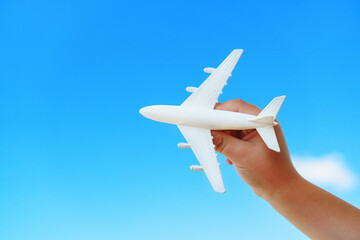 A white toy plane in a child's hand against a blue sky.