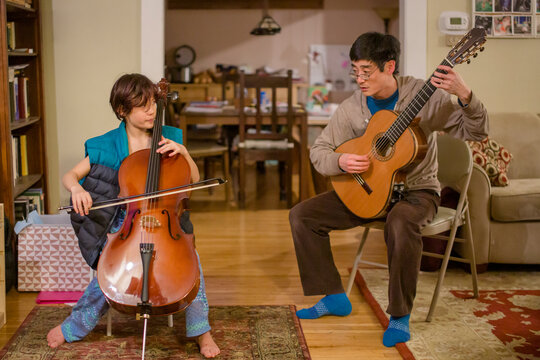 a tween boy and his father play music together in living room at home
