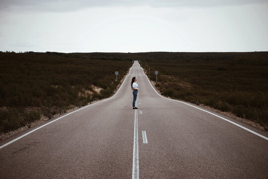 Young Spanish girl, in the middle of a lonely road, during summer.