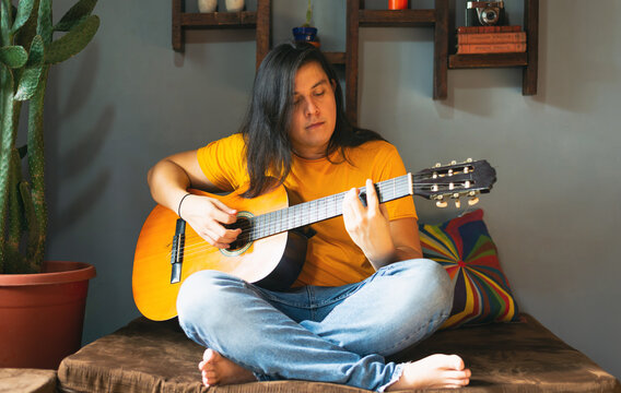 man with long hair, playing relaxed guitar at home during quarantine