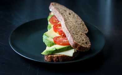 Healthy sandwich with cheese, avocado and tomato on a black plate