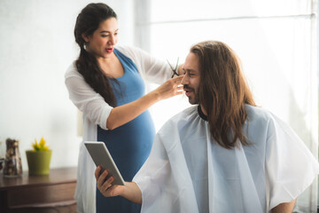 Obraz premium Couple having hair cut at home during quarantine coronavirus pandemic, online hairdressing on tablet