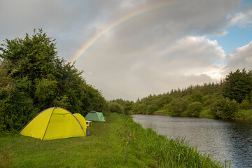 Wild camping on the bank of the river with rainbow in the background. Ireland