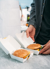 A guy in a gray shirt opens a paper box with a vegan burger. A food package with a food delivery in the background..