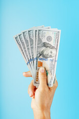A hand with one hundred-dollar bills on a blue background.