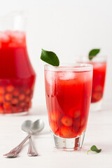 Summer delicious refreshing compote of cherries with pulp and with ice in glasses on a white background, a jug with a drink