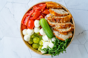 Take Away Healthy Organic Spicy Chicken Bowl with Mozzarella Balls, Spinach, Vinaigrette Dressing Sauce,  Cucumber, Pesto Sauce and Cherry Tomatoes in Plastic Box, Package / Container.