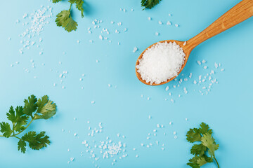 Sea salt in a wooden spoon on Large salt crystals with greens on a blue background.
