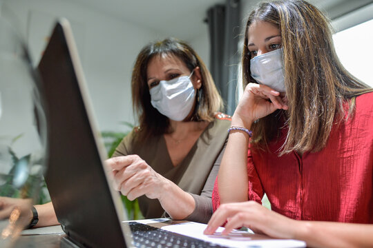 Student and her teacher wearing protective mask and working a lesson on  a laptop at home during lockdown due to covid-19