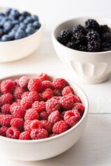 Raspberries, blueberries and blackberries close-up in bowls on a white background, ripe juicy berries