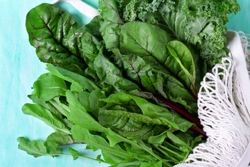 Chard, kale and arugula in the mesh bag on the green table. Top view. Organic fresh products