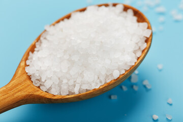Large sea salt crystals in a wooden spoon with greens on a blue background. Universal spice, free space
