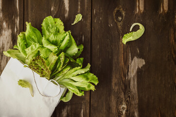 Lettuce leaveson in a paper bag a wooden dark table. Batavia salad. Authentic still life with green...