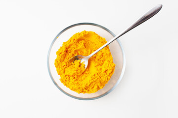 Spoon with turmeric spices in a bowl on a white background.