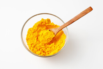 Bright yellow turmeric powder in a bowl with a wooden spoon on a white background.