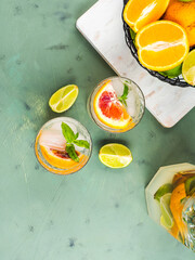 Fresh summer citrus lemonade with lime, mint, blood oranges and ice cubes in jar and glasses over...