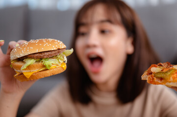 Hungry young woman eating junk food hamburger and pizza for lunch by ordering delivery at home on holiday. unhealthy meal, obesity risk.