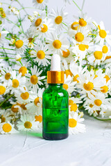 A glass dropper bottle of green color against a background of fragrant field daisies. Natural cosmetics and skin care. Aroma essential oil.