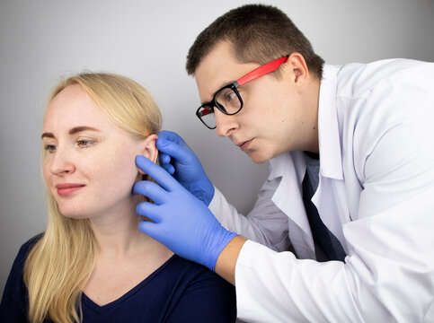 An otolaryngologist examines the ear of a girl who complains of pain. Pain relief and treatment concept. Inflammation of the ear canal or eardrum
