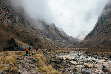 Trekkers with a guide traversing a valley on the Himalayan Annapurna Base Camp trek route near a mountain river