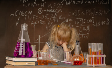 Curious little girl with test tubes and colorful substances makes tests at school laboratory. Small kid learning chemistry and conducts science experiment on biology lesson. Biology education concept.