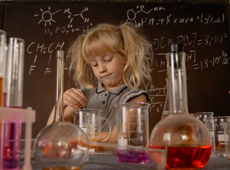 Little blonde girl doing science experiment and stirring orange liquid in laboratory glass