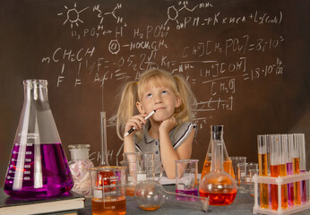 Curious little girl with test tubes and colorful substances makes tests at school laboratory. Small kid learning chemistry and conducts science experiment on biology lesson. Biology education concept.