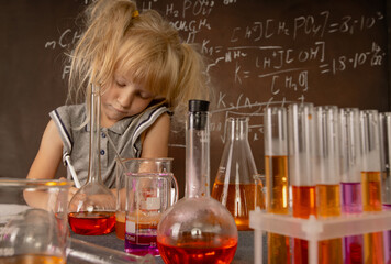 Curious little girl with test tubes and colorful substances making tests and taking notes at school laboratory. Small kid learning chemistry. Biology education concept.