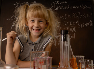 Funny smiling little girl with test tubes and colorful substances makes tests at school laboratory. Small kid learning chemistry and conducts experiment on lesson. Biology education concept.