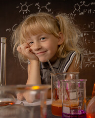 Curious little girl with test tubes and colorful substances with hand to her face makes tests at school laboratory. Small kid conducts science experiment on biology lesson. Biology education concept.