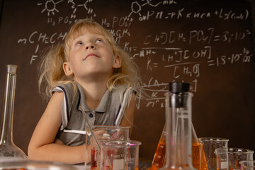 Curious little girl with test tubes and colorful substances makes tests at school laboratory. Small kid learning chemistry and conducts science experiment on biology lesson. Biology education concept.