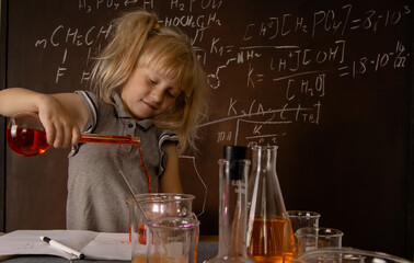 Curious little blonde girl with test tubes pouring orange colorful liquid into laboratory glass. Small kid observes chemical reaction. Biology education concept.