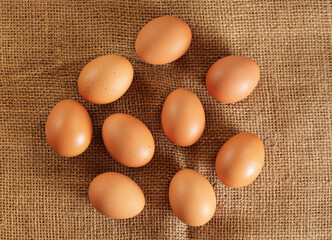 Nine beige coloured eggs on jute textile cloth, closeup view form above