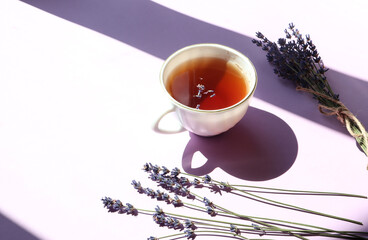  Dry branches and lavender flowers with a Cup of fragrant tea in the sun, on a lilac background, a...