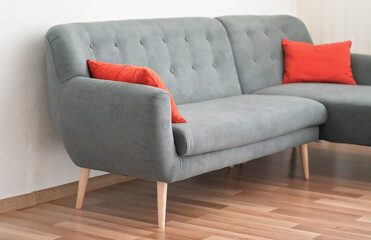 Modern gray couch with red pillows on wooden tiled floor - office furniture