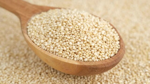 quinoa seeds in wooden spoon and on background rotating, top view