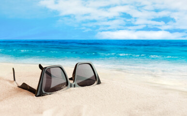 Fototapeta na wymiar Sunglasses on the seashore, tropical beach vacation background .