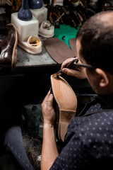 Obraz premium Male cobbler sitting at his shop and repairing man's shoe, brushing glue over sole.